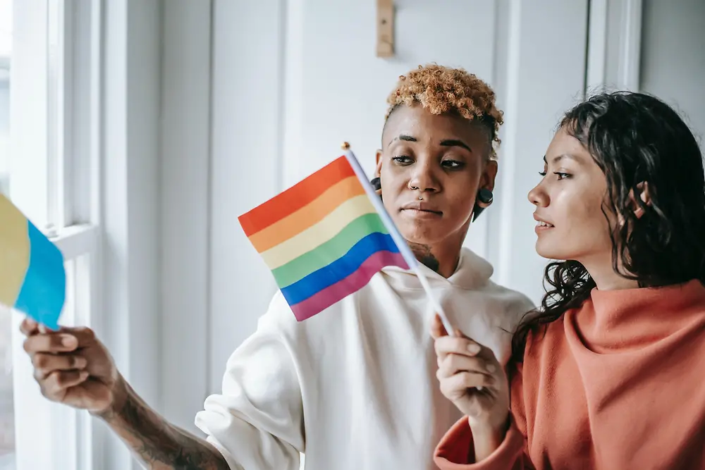 두 여성이 LGBTQ+ 깃발을 들고 서로 이야기를 나누고 있습니다.