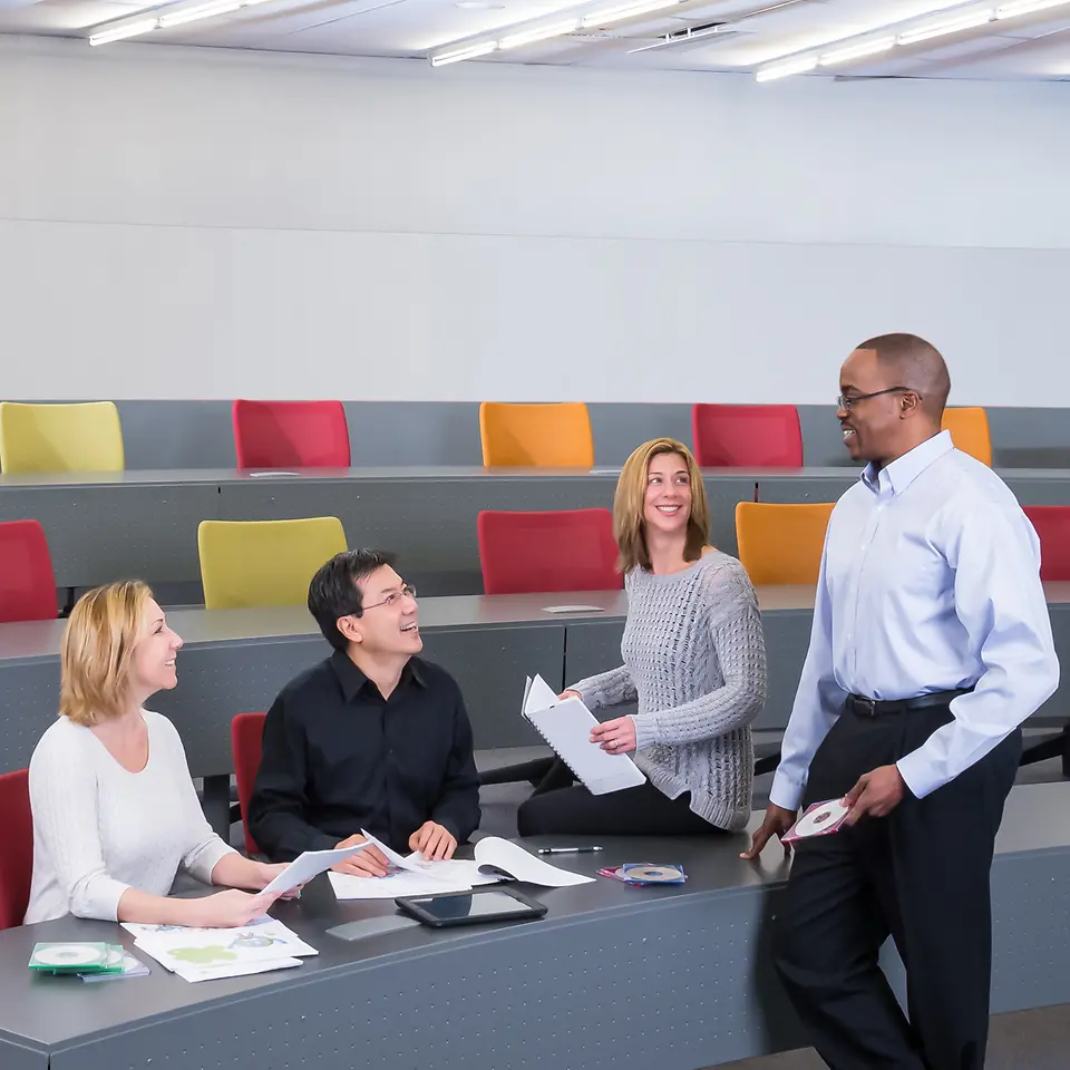 A standing employee is talking to three sitting employees.